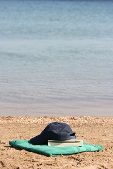 blue baseball hat on green towel by the see and book