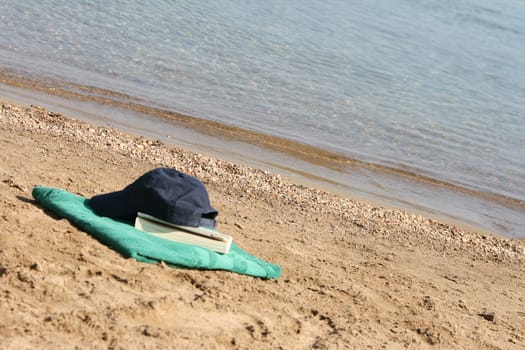 blue baseball hat on green towel by the see and book