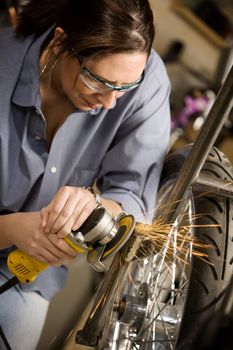 Hispanic womman using grinder tool on the front fork of motorcycle
