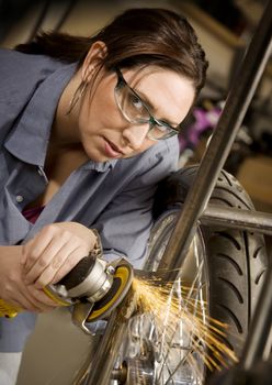 Hispanic woman using grinder tool on the front fork of motorcycle