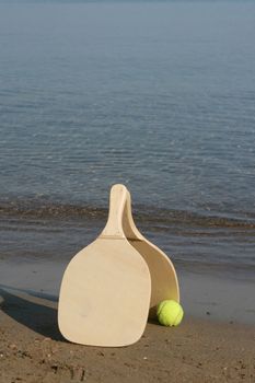 two wooden beach rackets by the shore with yellow ball