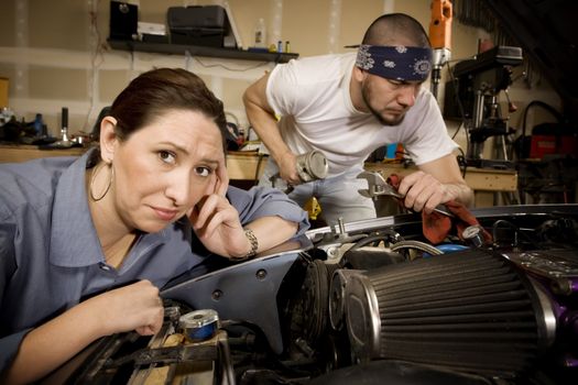 Bored woman leaning on car with male mechanic ignoring her in background