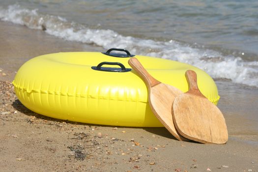 yellow  inflatable by the sea and wooden beach tennis rackets