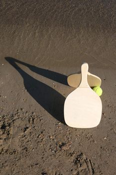 two wooden beach rackets by the shore with yellow ball