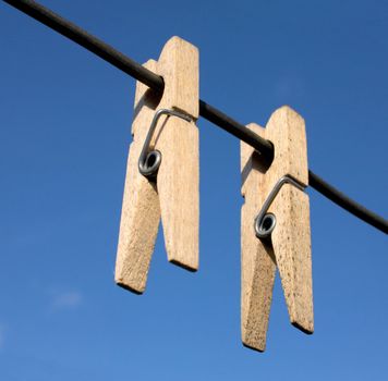 Two wooden clothes-peg hang a rope on sky background