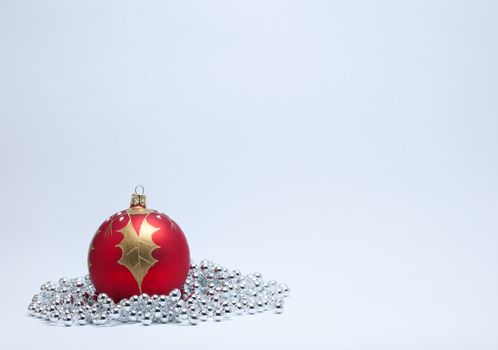 Single red and gold Christmas bauble with a gold holly leaf and silver beads on a white background.