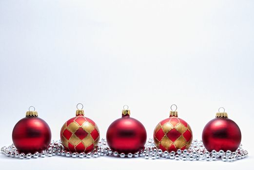 Red and gold Christmas baubles with silver beads on a white background.