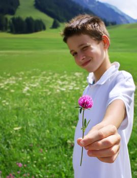Boy in mountainous environment giving wild flower.