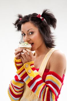 Beautiful Latina girl with huge eyes open holding a cupcake and biting it, isolated