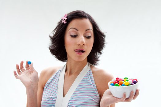 Happy beautiful candy girl with a bowl of colorful bubblegum candy balls licking her lip, isolated