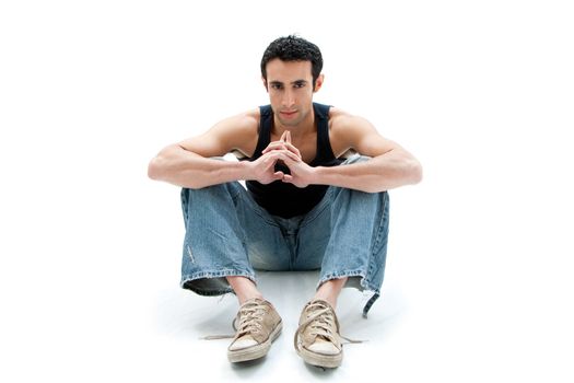 Handsome Caucasian guy wearing black tank top and jeans sitting on floor thinking, isolated