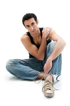 Handsome Caucasian guy wearing black tank top and jeans sitting on floor holding shoulder, isolated