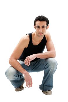 Handsome serious Caucasian guy wearing black tank top and jeans squatting, isolated