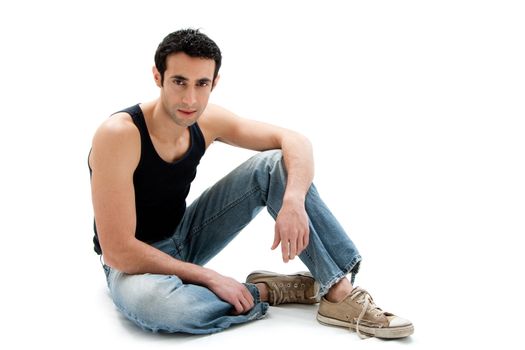 Handsome Caucasian guy wearing black tank top and jeans sitting on floor, isolated