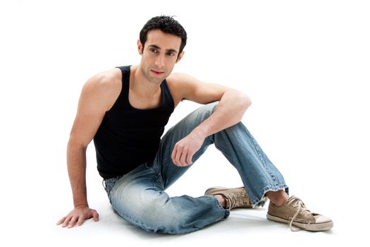 Handsome Caucasian guy wearing black tank top and jeans sitting on floor, isolated