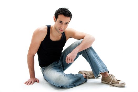 Handsome Caucasian guy wearing black tank top and jeans sitting on floor looking down, isolated