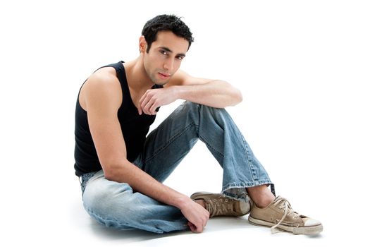 Handsome Caucasian guy wearing black tank top and jeans sitting on floor, isolated