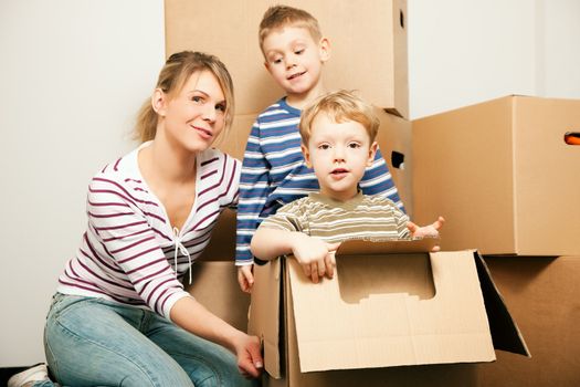 Family moving in their new house. The sons are sitting inside the moving boxes, everybody is looking rather cheerful
