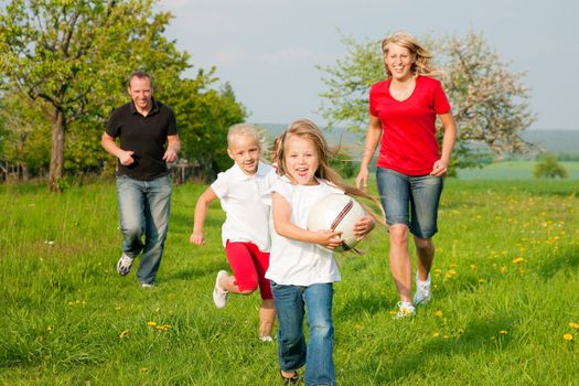 Happy family playing football, one child has grabbed the ball and is being chased by the others