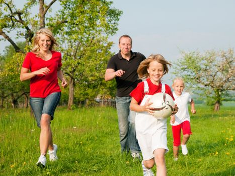Happy family playing football, one child has grabbed the ball and is being chased by the others