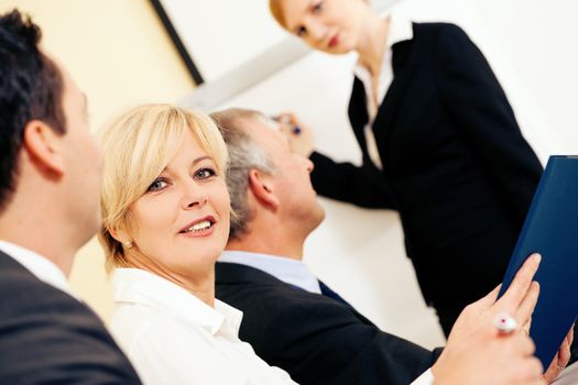 Business team receiving a presentation held by a female co-worker standing in front of a flipchart