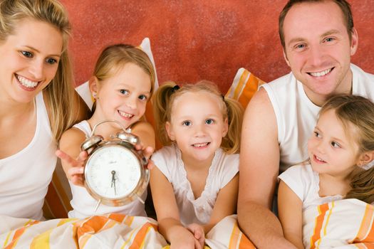 Family in bed in the morning, on child holding a clock – metaphor for getting up to enjoy the day
