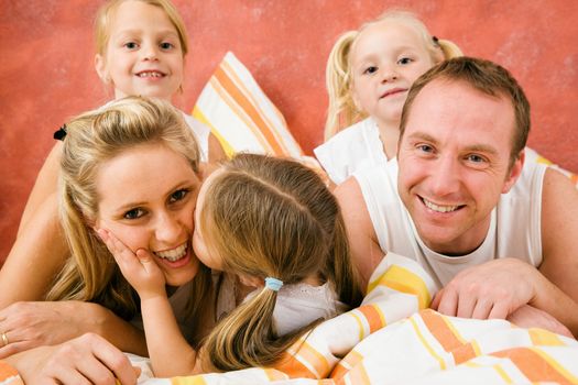 Family in bed in the morning, daughter kissing and hugging her mother