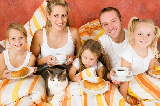 Family of five and their cat having breakfast in their bed in the morning