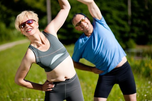 Mature or senior couple in jogging gear doing sport and physical exercise outdoors, stretching and gymnastics