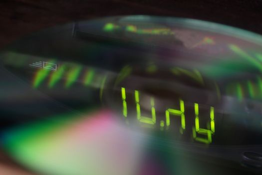 A closeup of dvd with the lights from a digital display reflecting on them.  Note the focus is on the digits.
