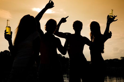 People (two couples) on the beach dancing to music, drinking and having a lot of fun in the sunset - only silhouette of people to be seen