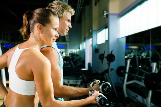 couple in the gym, rivaling each other, exercising with weights (focus on the face of the girl)