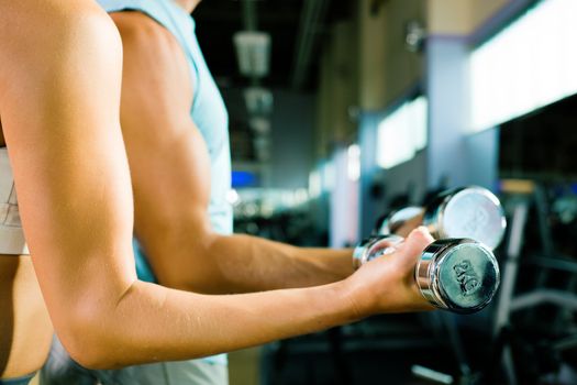 man and a woman (only arms and body) lifting dumbbells (focus on dumbbell, shallow depth of field)