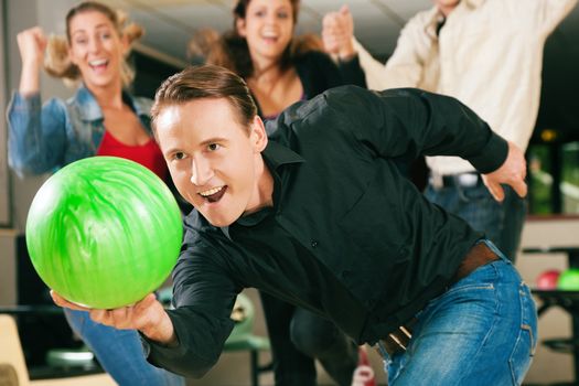 Group of four friends in a bowling alley having fun, three of them cheering the one in charge to throw the ball