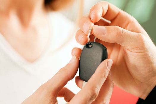 Woman at a car dealership buying an auto, the sales rep giving her the key, macro shot with focus on hands and key
