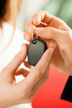 Woman at a car dealership buying an auto, the sales rep giving her the key, macro shot with focus on hands and key