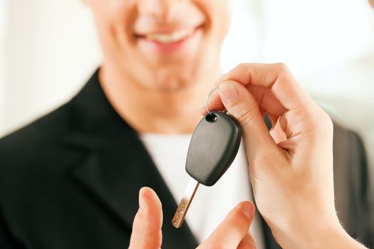 Man at a car dealership buying an auto, the female sales rep giving him the key, macro shot with focus on hands and key