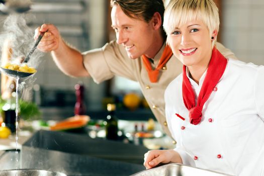 Two chefs in teamwork - man and woman - in a restaurant or hotel kitchen cooking delicious food, he is taking out the pasta