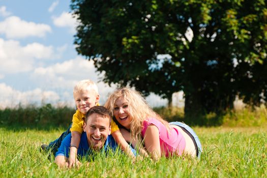 Young family having fun in the sun lying on the meadow an a bright summer day