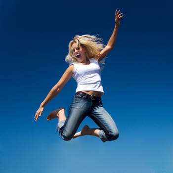 A young and beautiful woman jumping into a perfect blue sky