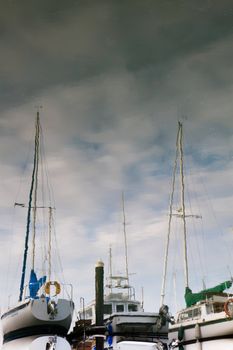 Reflections of sailboats in still water with partly cloudy skies