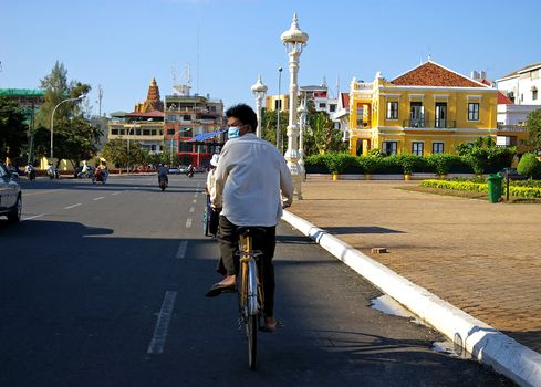 A Cambodian man cycling in the capital city, wearing a face mask, Phnom Penh, Cambodia is one of several Asian countries taking part in the Kitakyushu Initiative for a Clean Environment. 