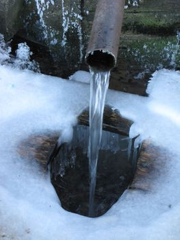 Running water from metal pipe, winter, ice-covered background