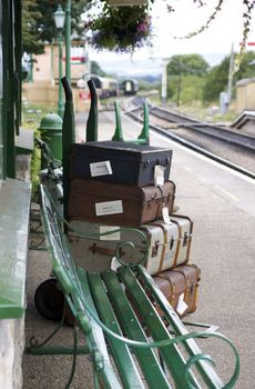 A set of period luggage with labels, consisting of old leather cases, set on a trolly on the platform of a retro railway station. Location at Harmans Cross station on the Swanage steam railway network in Dorset.