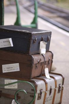 A set of period luggage consisting of old leather cases, set on a trolly on the platform of a retro railway station. Location at Harmans Cross station on the Swanage steam railway network in Dorset.