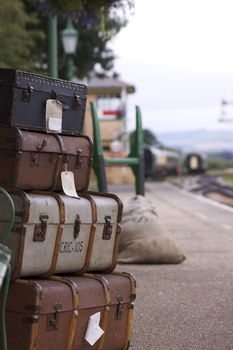 A set of labeled period luggage consisting of old leather cases, set on a trolly on the platform of a retro railway station. Location at Harmans Cross station on the Swanage steam railway network in Dorset. The stations signal box and carriages in soft focus to the background.