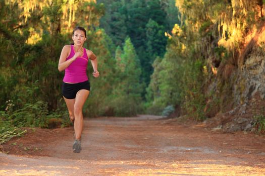 Female athlete running on forest road - copy space. Chinese Asian / Caucasian female woman runner.