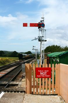 A period railway signal at the end of the platform at Harmans Cross station, part of the Swanage steam railway network in Dorset. Period railway carriages are visible in the background.