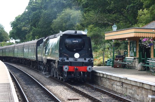 A steam train arriving at Harmans Cross station, part of the Swanage Steam Railway system in Dorset. Visible to the foreground is the station waiting room.
