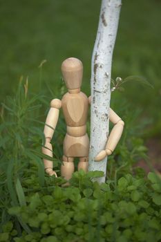 Little wooden toy man hugging a tree